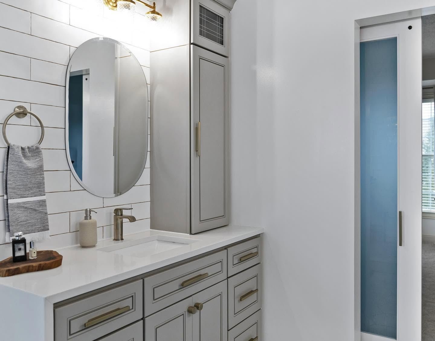 The bathroom after: grey vanity with brass pulls, linen tower, oval mirror and white tile