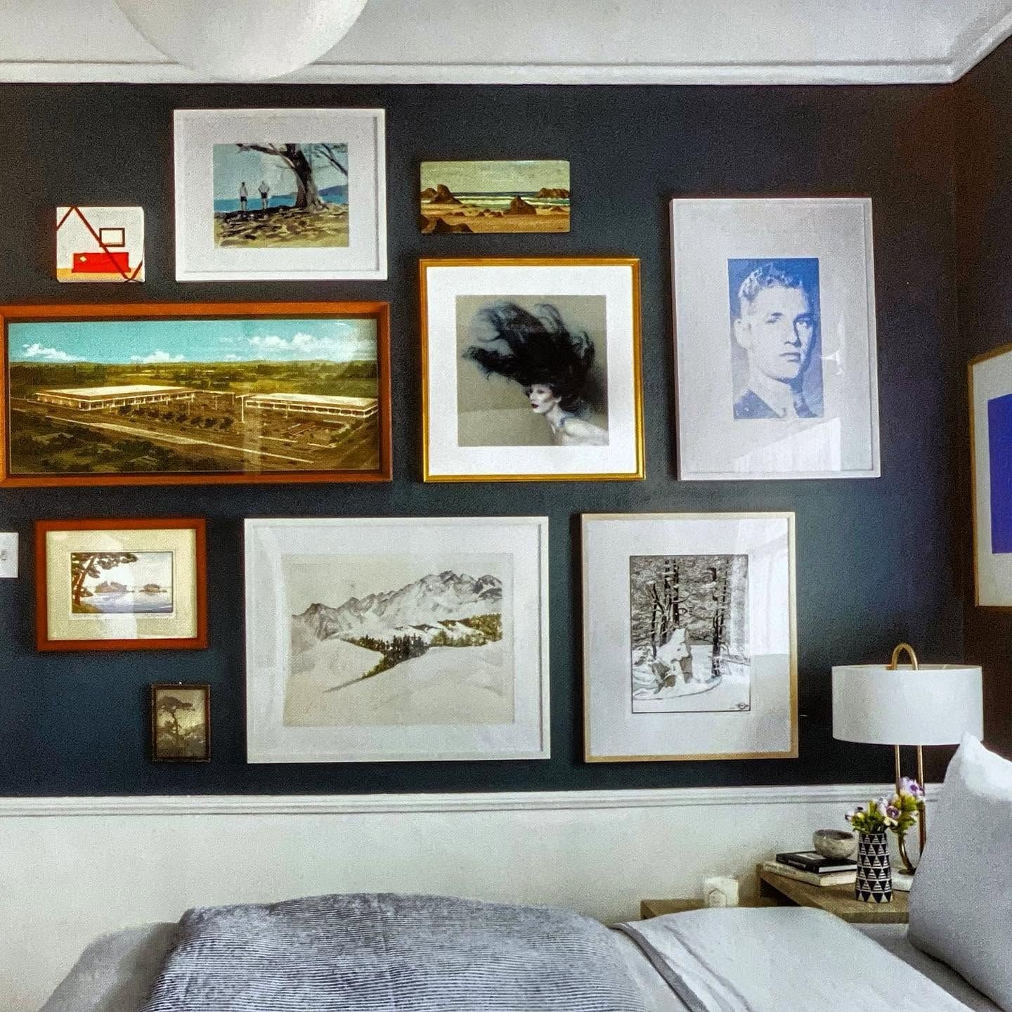 Gallery wall of framed art on a deep navy wall above a bed
