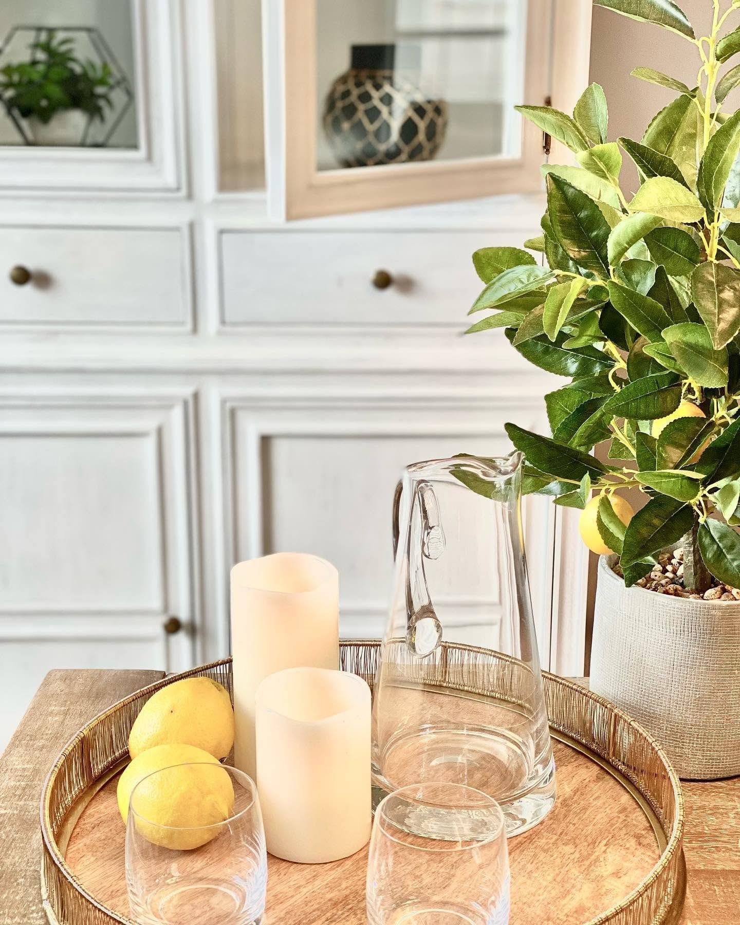 Tray with lemons, candles and a glass pitcher beside a lemon tree