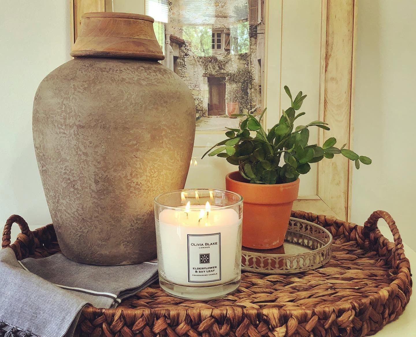 Earthenware urn, candle and potted plant on a woven tray