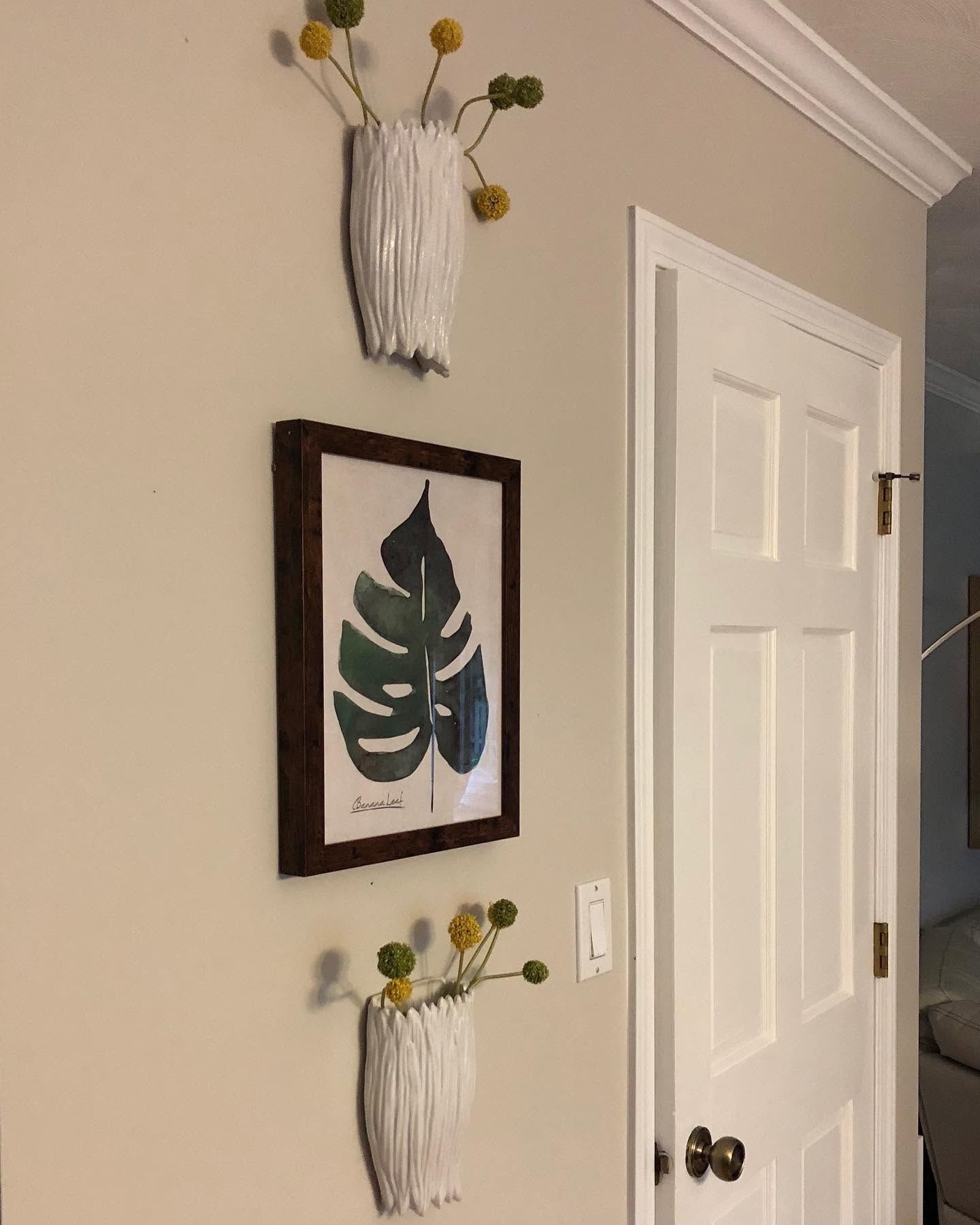 Wall-mounted white vases with billy balls around a framed leaf print